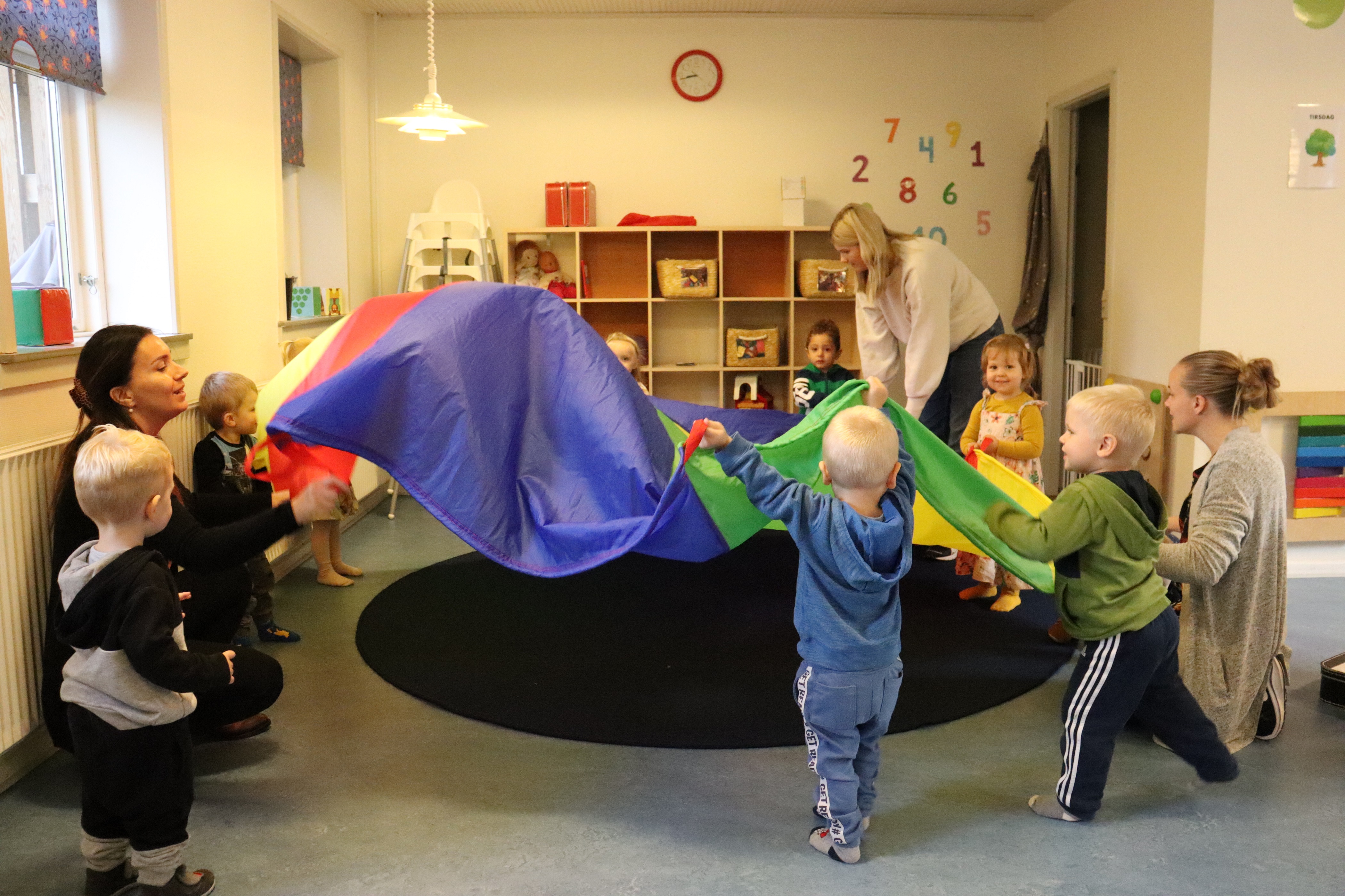 Børn leger med faldskærms tæppe indenfor 